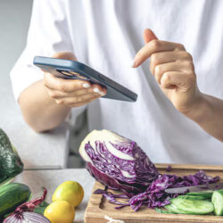 woman-uses-smartphone-kitchen-while-preparing-vegetable-salad_169016-49843
