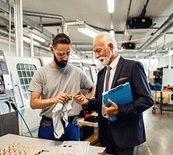 senior-quality-control-inspector-young-worker-cooperating-while-analyzing-manufactured-products-factory-plant