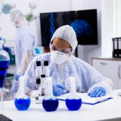 female-scientist-protection-equipment-taking-notes-with-smoking-blue-solution-test-tubes (1)
