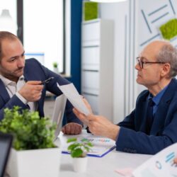 senior-entrepreneur-discussing-with-coworker-holding-documents-conference-briefing-businessman-discussing-ideas-with-colleagues-about-financial-strategy-new-start-up-company (1) (1) (1)